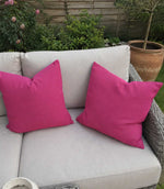 Two pink cushions on a beige outdoor sofa with a garden background
