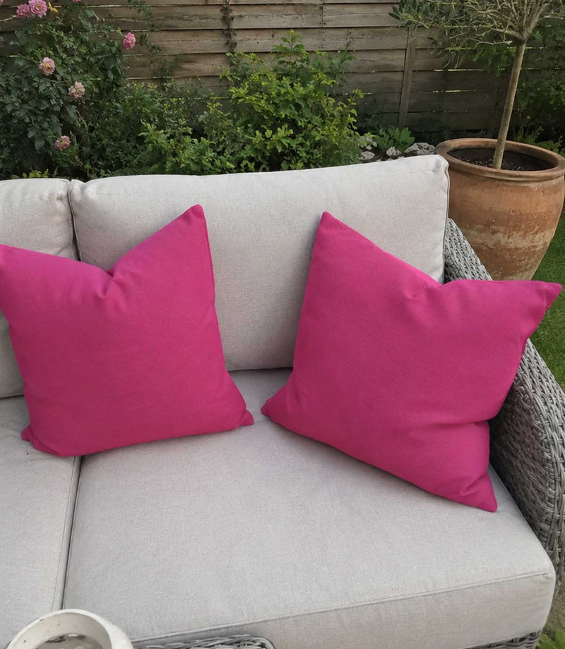 Two pink cushions on a beige outdoor sofa with a garden background