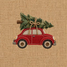 Embroidered design of a red vintage car carrying a green Christmas tree on its roof, stitched on a beige burlap fabric background.