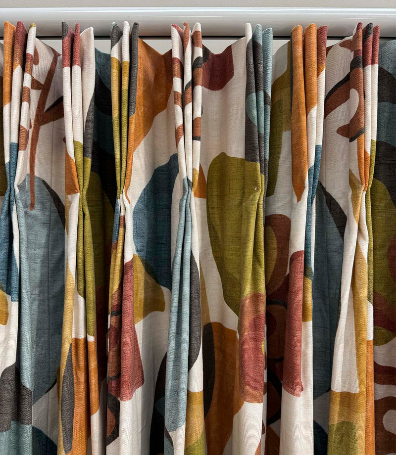 Close-up of Elaris Fabric Auburn curtains with a bold abstract botanical design in burnt orange, teal blue, olive green, rust and charcoal on a natural cream background.
