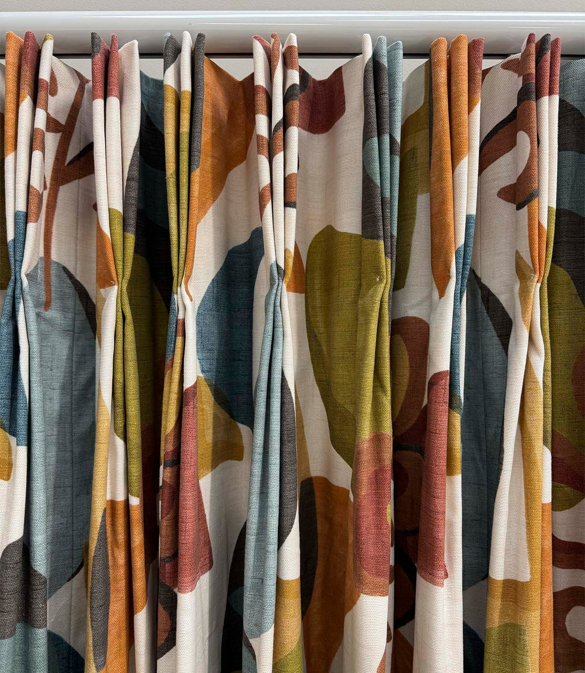 Close-up of Elaris Fabric Auburn curtains with a bold abstract botanical design in burnt orange, teal blue, olive green, rust and charcoal on a natural cream background.