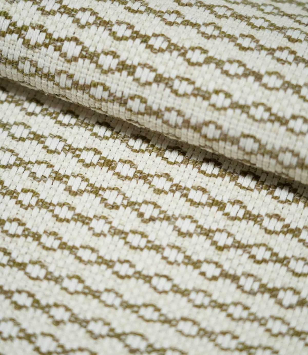 Close-up of folded Elkstone Matcha fabric showing its structured woven texture and small-scale olive green geometric motifs against a natural cream base.