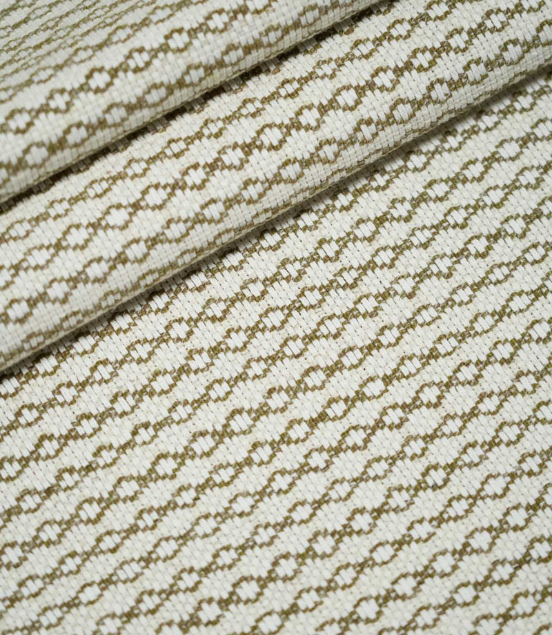Elkstone Matcha woven fabric arranged in soft, overlapping folds, displaying its repeating olive green geometric pattern and textured cream surface.