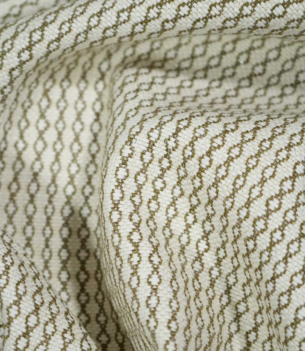 Elkstone Matcha fabric loosely gathered into deep folds, showing the continuous olive green geometric pattern woven into a textured natural cream background.