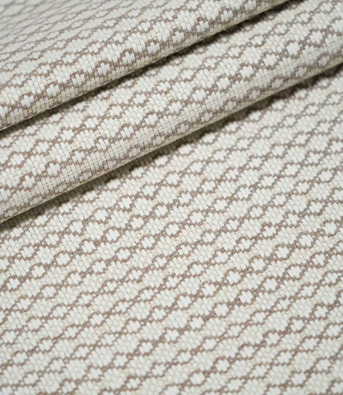 Elkstone Taupe woven fabric arranged in overlapping folds, displaying its repeating taupe geometric pattern and textured natural cream surface.