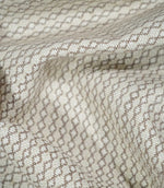 Elkstone Taupe fabric loosely gathered into curved folds, showing the continuous taupe linked geometric pattern woven into a natural cream background.