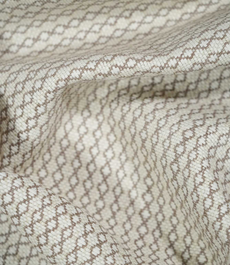Elkstone Taupe fabric loosely gathered into curved folds, showing the continuous taupe linked geometric pattern woven into a natural cream background.