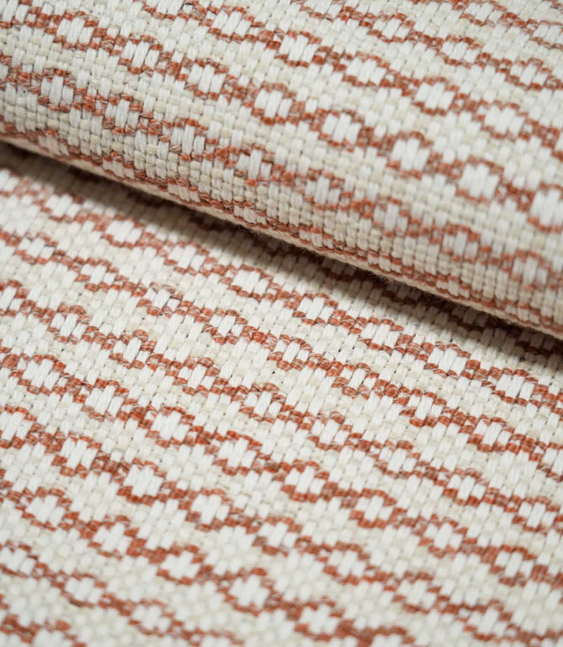 Close-up of folded Elkstone Terracotta fabric showing its structured woven texture, raised cream yarns and small-scale terracotta geometric motifs.