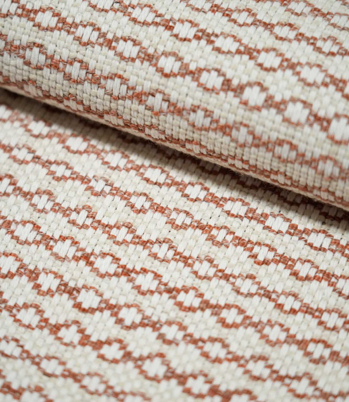 Close-up of folded Elkstone Terracotta fabric showing its structured woven texture, raised cream yarns and small-scale terracotta geometric motifs.