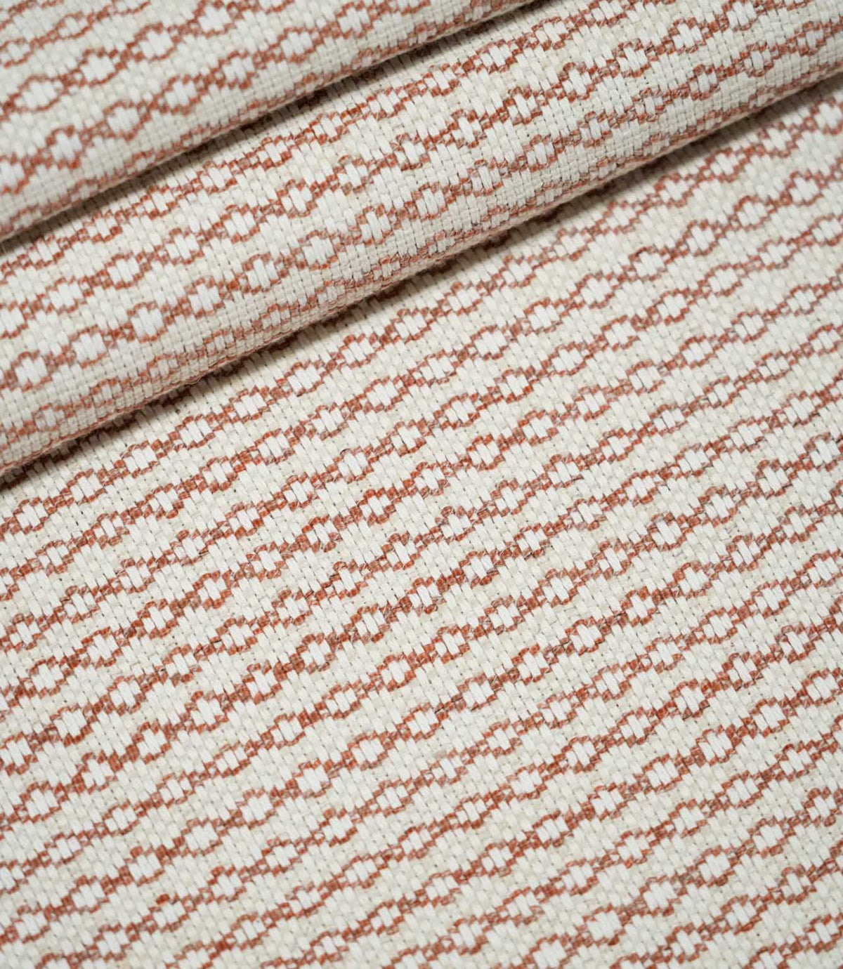 Elkstone Terracotta woven fabric arranged in soft, overlapping folds, displaying its repeating rust-orange geometric pattern and textured natural cream surface.