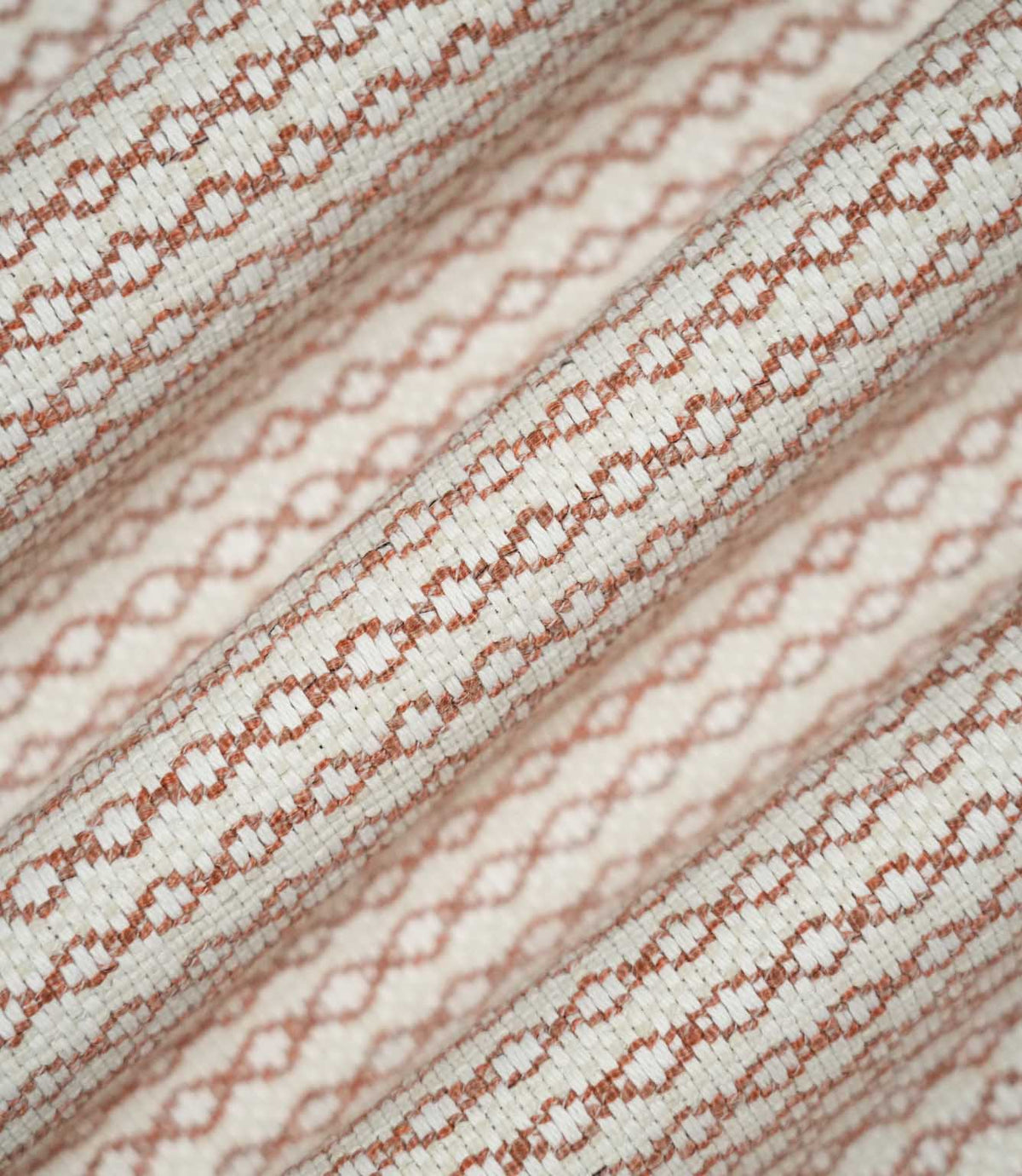 Detailed view of Elkstone Terracotta fabric gathered into flowing folds, highlighting its tactile woven texture and repeating terracotta geometric design.