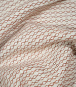 Elkstone Terracotta fabric loosely gathered into deep, curved folds, showing the continuous rust-orange linked geometric pattern woven into a natural cream background.