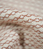 Extreme close-up of Elkstone Terracotta upholstery fabric revealing interwoven cream and terracotta yarns, a raised textured surface and repeating small-scale geometric motifs.