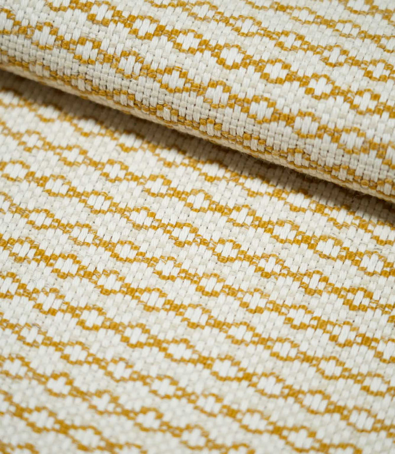Close-up of folded Elkstone Turmeric fabric showing its chunky woven texture, raised cream yarns and repeating mustard yellow geometric motifs.