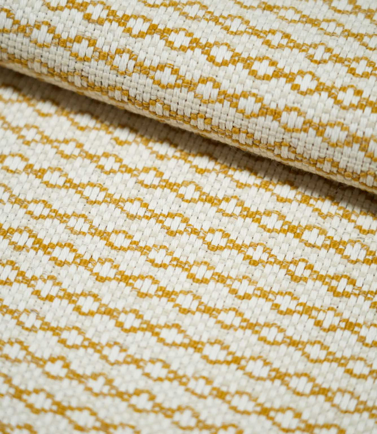Close-up of folded Elkstone Turmeric fabric showing its chunky woven texture, raised cream yarns and repeating mustard yellow geometric motifs.
