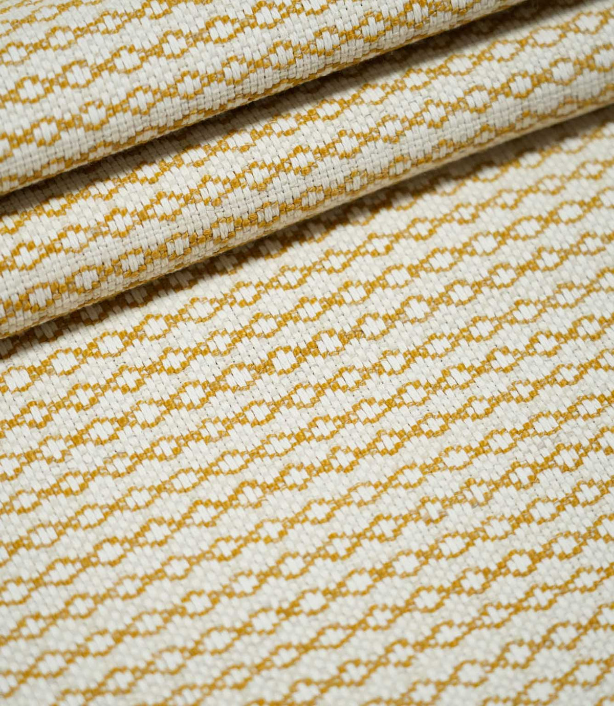 Elkstone Turmeric woven fabric arranged in overlapping folds, displaying its repeating golden yellow geometric pattern and textured natural cream surface.