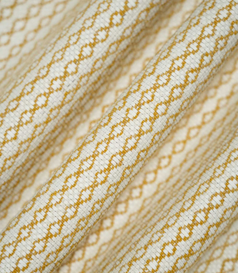 Detailed view of Elkstone Turmeric fabric gathered into soft folds, highlighting its tactile woven texture and small-scale geometric design in mustard yellow and cream.