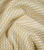Elkstone Turmeric fabric loosely gathered into curved folds, showing the continuous golden yellow linked geometric pattern woven into a natural cream background.