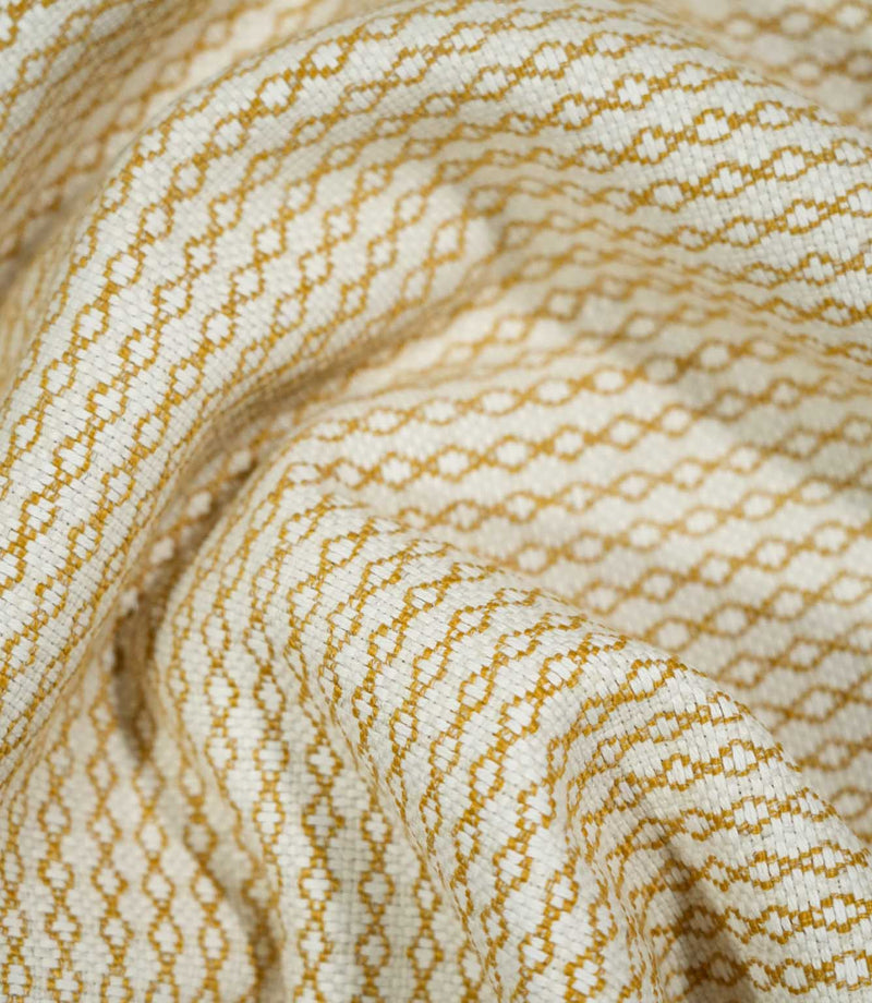 Elkstone Turmeric fabric loosely gathered into curved folds, showing the continuous golden yellow linked geometric pattern woven into a natural cream background.