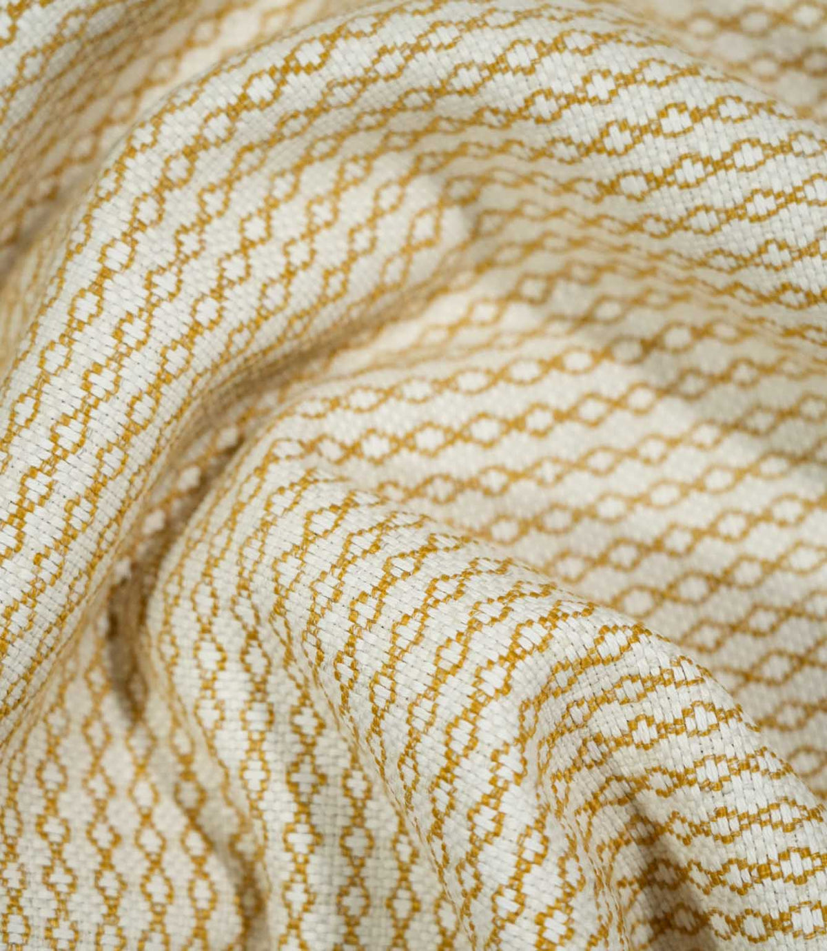 Elkstone Turmeric fabric loosely gathered into curved folds, showing the continuous golden yellow linked geometric pattern woven into a natural cream background.