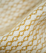 Extreme close-up of Elkstone Turmeric fabric revealing interwoven cream and golden mustard yarns, a raised textured surface and repeating small-scale geometric motifs.