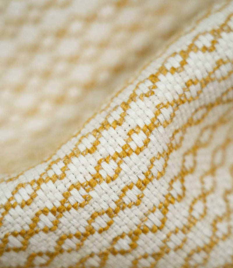 Extreme close-up of Elkstone Turmeric fabric revealing interwoven cream and golden mustard yarns, a raised textured surface and repeating small-scale geometric motifs.