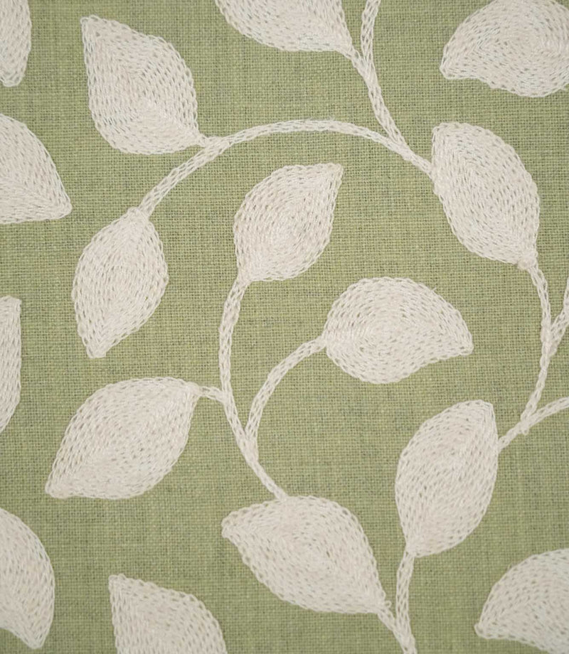 Detailed close-up of Ellerton Apple fabric showing raised cream leaf embroidery connected by delicate curved stems on an apple green woven ground, highlighting the individual stitches, tactile embroidery and subtle texture of the base fabric.