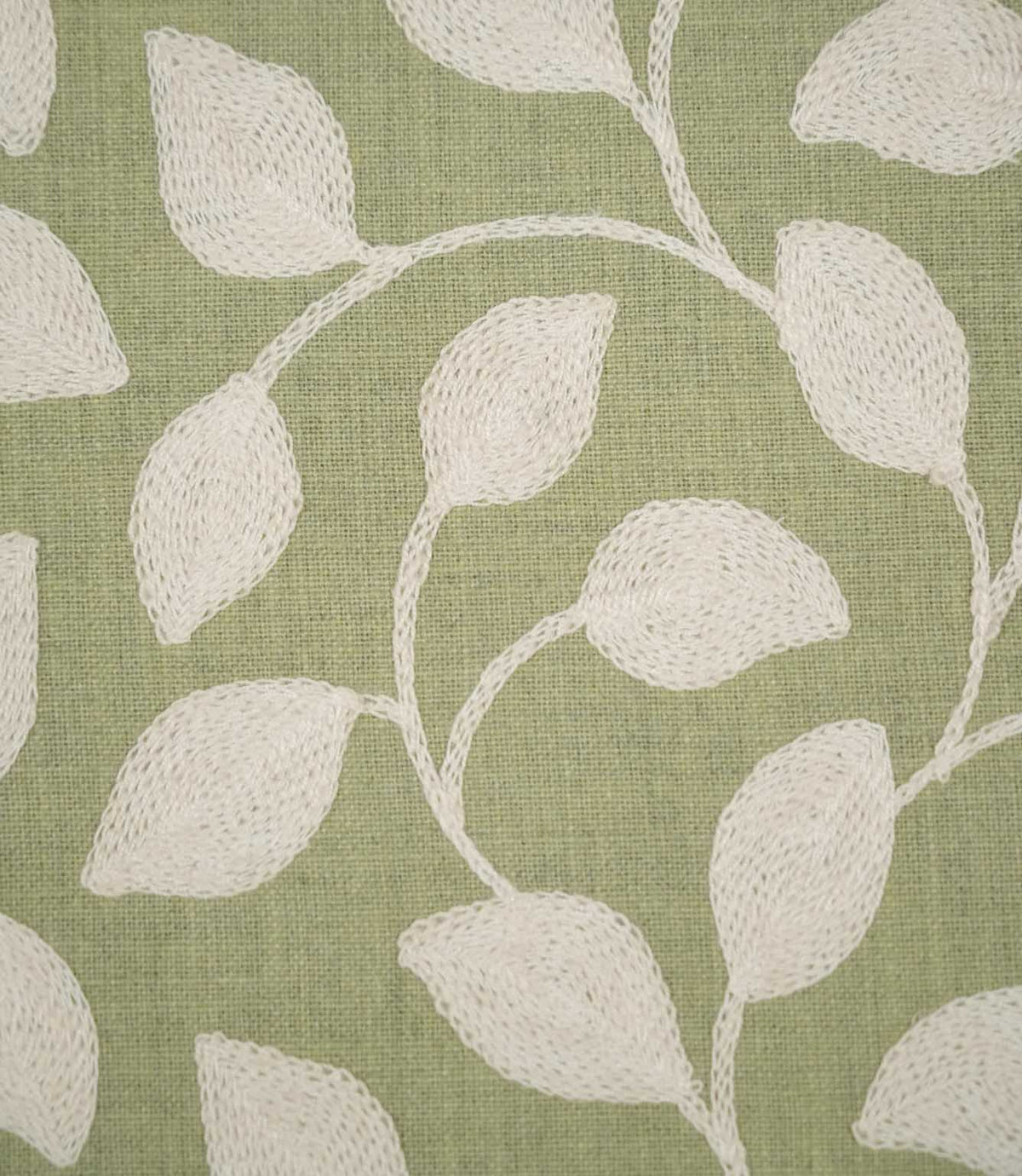 Detailed close-up of Ellerton Apple fabric showing raised cream leaf embroidery connected by delicate curved stems on an apple green woven ground, highlighting the individual stitches, tactile embroidery and subtle texture of the base fabric.