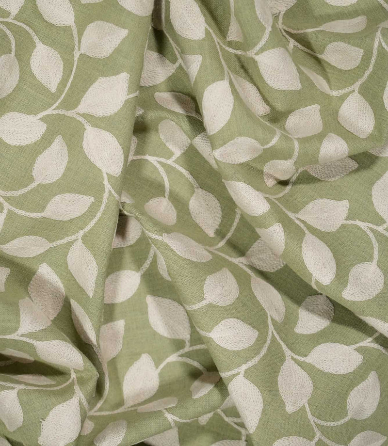 Ellerton Apple embroidered fabric loosely draped into soft folds, showing the repeating cream foliage design flowing across an apple green ground and demonstrating the fabric's natural drape and textured finish for curtains, blinds, cushions and decorative upholstery.