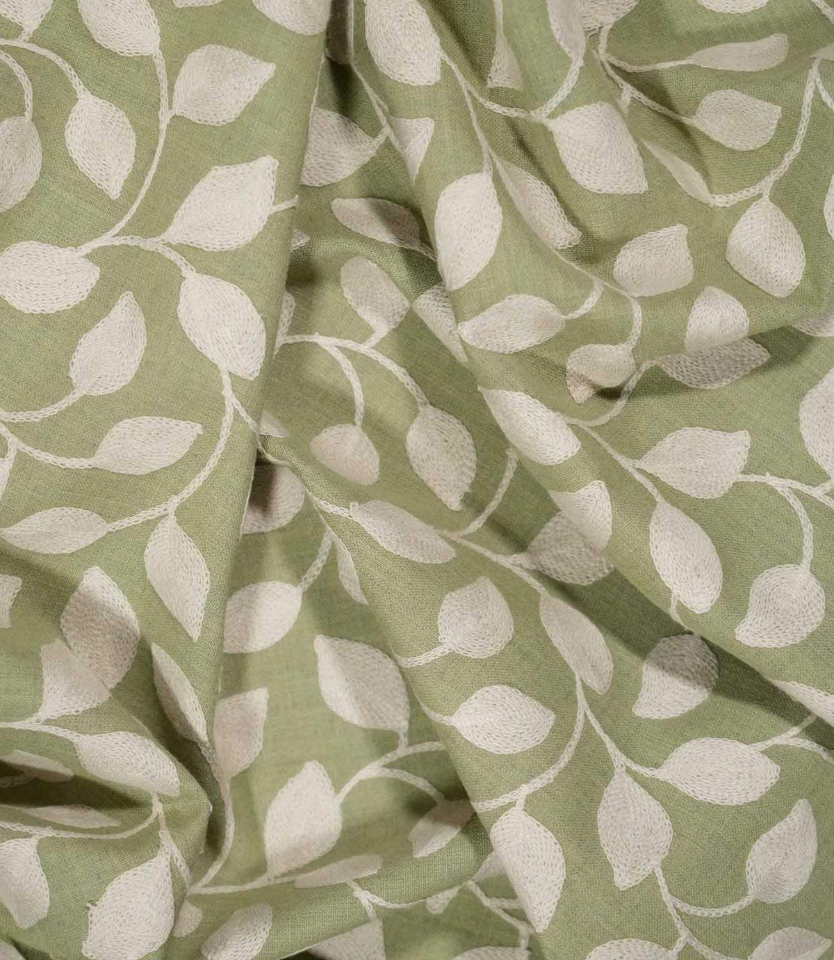 Ellerton Apple embroidered fabric loosely draped into soft folds, showing the repeating cream foliage design flowing across an apple green ground and demonstrating the fabric's natural drape and textured finish for curtains, blinds, cushions and decorative upholstery.