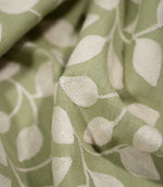 Detailed close-up of Ellerton Apple fabric gathered into soft sculptural folds, focusing on the raised cream embroidered leaves, fine stitched stems and textured apple green woven background, clearly showing the depth and tactile character of this contemporary foliage fabric.