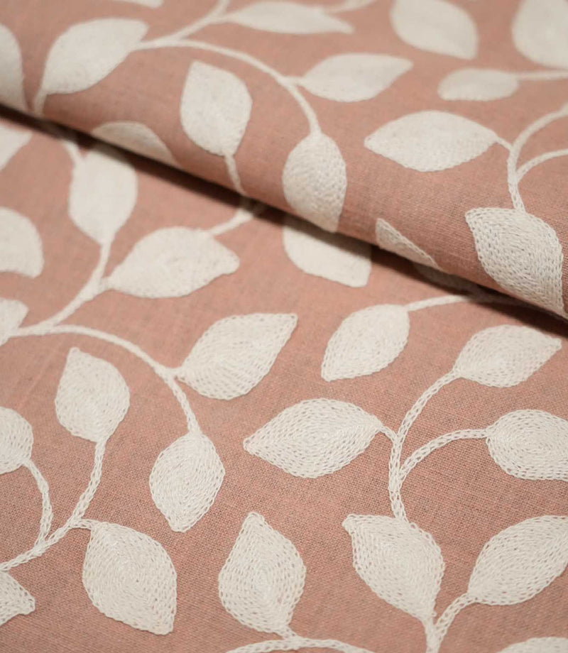 Close-up of folded Ellerton Blush fabric showing the cream embroidered leaf and trailing vine pattern continuing across a blush pink woven ground, with the fold demonstrating the fabric's structure, thickness and softly textured finish.
