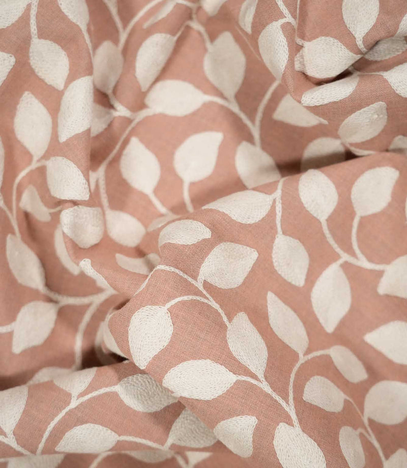Ellerton Blush fabric loosely draped into soft, flowing folds, showing the cream embroidered leaf and vine design across a warm blush pink background and demonstrating how the botanical pattern follows the fabric's natural drape and movement.