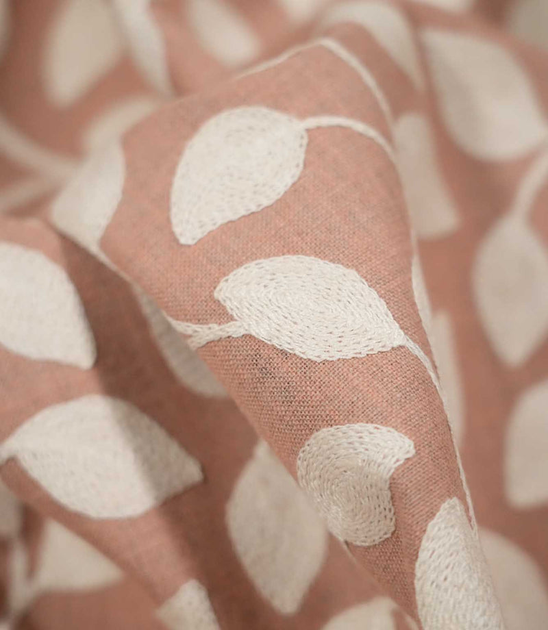 Macro close-up of Ellerton Blush fabric gathered into a soft fold, focusing on raised cream embroidered leaves and fine stitched stems against the textured blush pink woven ground, with a softly blurred background emphasising the depth and tactile quality of the embroidery.