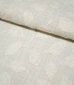 Close-up of folded Ellerton Cloud embroidered fabric showing ivory botanical leaves and gently winding stems across a pale neutral cloud-grey ground, with the soft fold highlighting the fabric's thickness, woven texture and raised embroidery.
