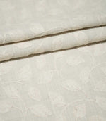 Ellerton Cloud fabric arranged in neat overlapping folds, showing the tonal ivory embroidered leaf and trailing vine pattern across a pale cloud-grey woven background, highlighting the subtle botanical design, tactile stitching and softly structured drape.