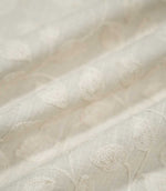 Close-up of Ellerton Cloud embroidered fabric arranged in gentle flowing folds, showing tonal ivory botanical leaves and trailing stems across a pale cloud-grey woven ground, with selective focus highlighting the raised embroidery and natural texture while the surrounding fabric softly fades out of focus.