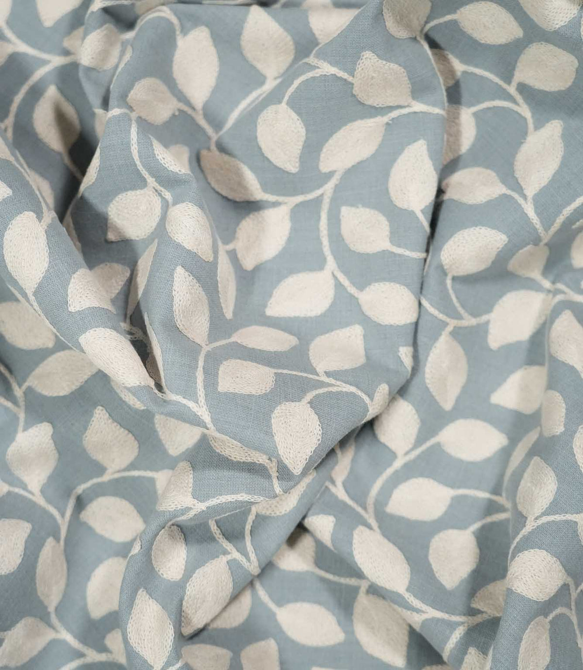 Ellerton Cornflower foliage fabric loosely draped into soft, natural folds, showing how the cream embroidered leaves and winding stems flow across the cornflower blue ground and demonstrating the fabric's drape for curtains, blinds and soft furnishings.