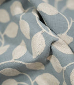 Detailed close-up of Ellerton Cornflower fabric gathered into sculptural folds, focusing on the raised cream embroidered leaves, fine stitched stems and cornflower blue woven background to show the depth, texture and tactile quality of the design.