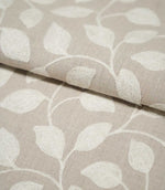 Close-up of folded Ellerton fabric showing cream embroidered leaves and flowing stems across a natural beige background, with the fold highlighting the fabric's woven texture and embroidered surface.