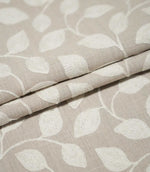 Ellerton fabric arranged in neat layered folds, displaying the repeating cream embroidered foliage design and natural beige woven ground while showing the fabric's thickness and texture.