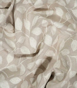 Ellerton embroidered fabric loosely draped into natural folds, showing how the cream trailing leaf pattern moves across the natural beige ground and demonstrating the fabric's soft handle and drape.