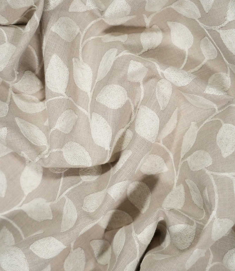Ellerton embroidered fabric loosely draped into natural folds, showing how the cream trailing leaf pattern moves across the natural beige ground and demonstrating the fabric's soft handle and drape.