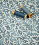 Elmsley blue floral fabric with two coordinating blue thread spools resting on the surface, showing the fabric's detailed print, texture and tonal blue palette.