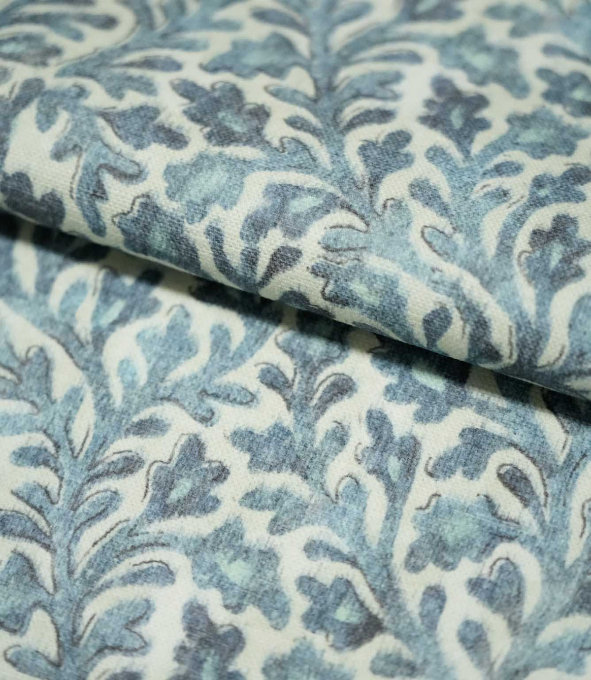 Folded Elmsley blue fabric showing the small-scale botanical pattern and woven surface texture, with blue and aqua foliage on a soft cream ground.