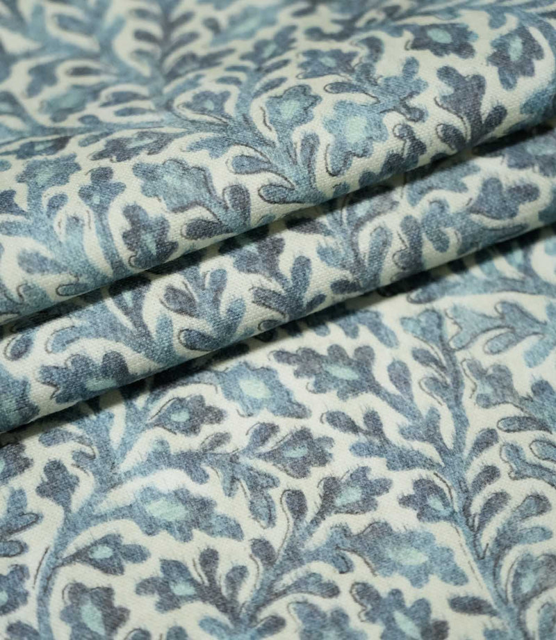 Layers of folded Elmsley blue fabric displaying the repeating floral and foliage design in tonal blue and aqua shades on a cream background.