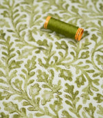 Elmsley Green floral fabric displayed with a coordinating olive green thread spool, showing the detailed foliage pattern, softly textured print and natural green tones against an off-white ground.