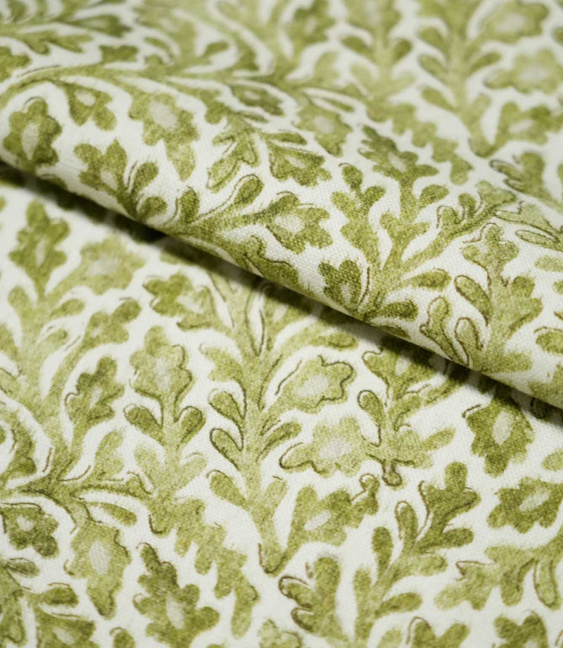 Close-up of folded Elmsley Green fabric showing the small-scale botanical pattern continuing across the folds, with olive and moss green leaves, delicate floral forms and softly outlined foliage on an off-white background.