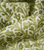 Detailed close-up of draped Elmsley Green fabric, highlighting the woven surface texture, softly printed olive and moss green leaves, stylised flowers and flowing foliage pattern against a warm off-white ground.