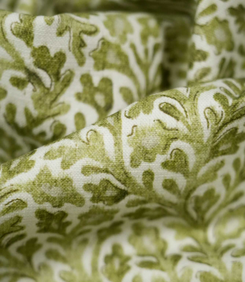 Detailed close-up of draped Elmsley Green fabric, highlighting the woven surface texture, softly printed olive and moss green leaves, stylised flowers and flowing foliage pattern against a warm off-white ground.